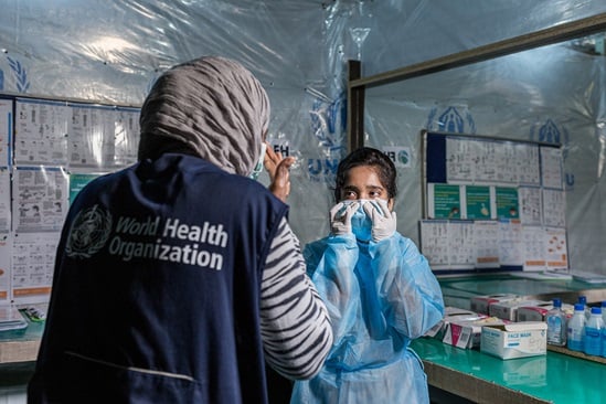 At a Severe Acute Respiratory Infection Isolation and Treatment Center facility, WHO Infection Prevention and Control Specialist Rebecca Rachel Apolot helps a nurse safely put on personal protective equipment before caring for patients with COVID-19.